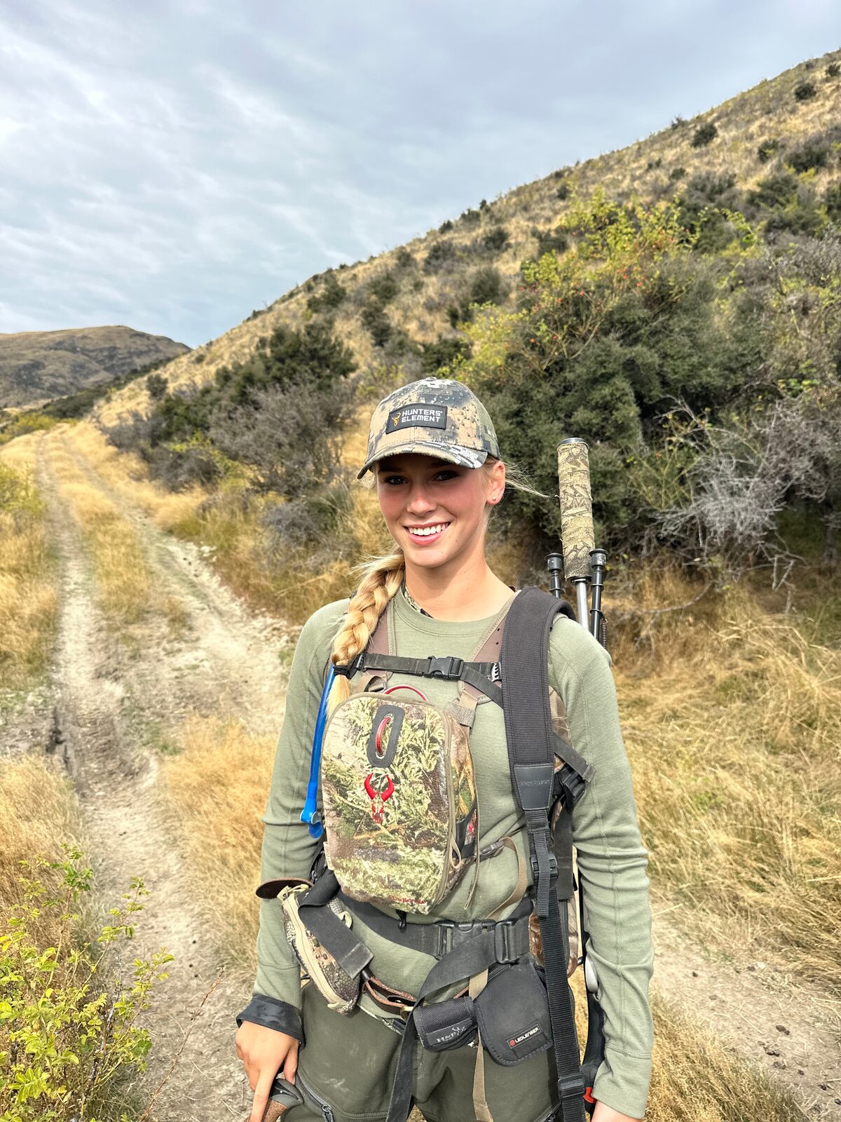 Suzy Toresen in hunting gear with a rifle on a track in the hills